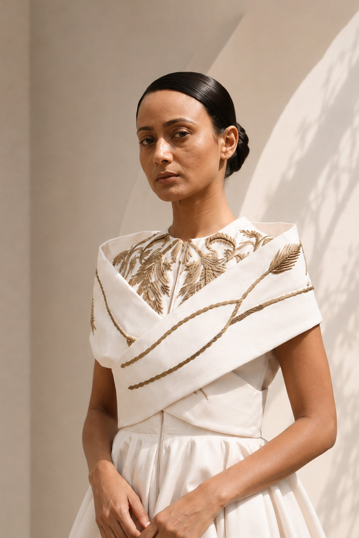 Ivory high-low dress featuring sculptural draped detailing, delicate embroidery, and a striking scarlet contrast lining for a bold yet refined statement.
