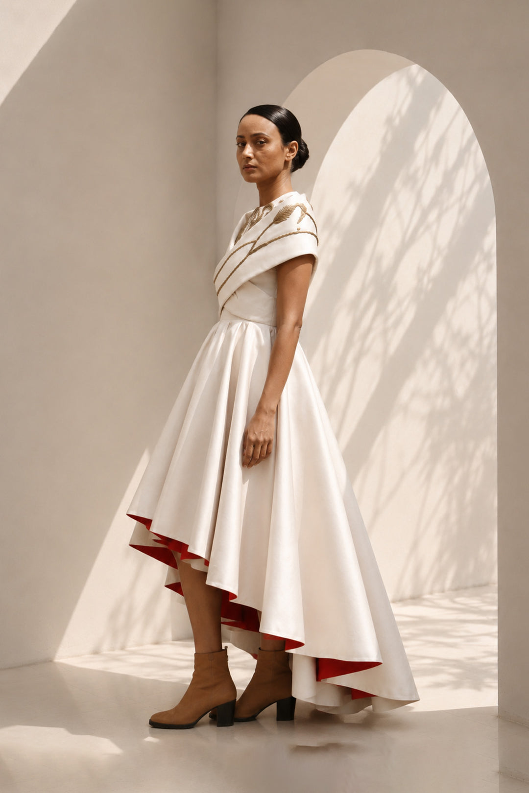 Ivory high-low dress featuring sculptural draped detailing, delicate embroidery, and a striking scarlet contrast lining for a bold yet refined statement.