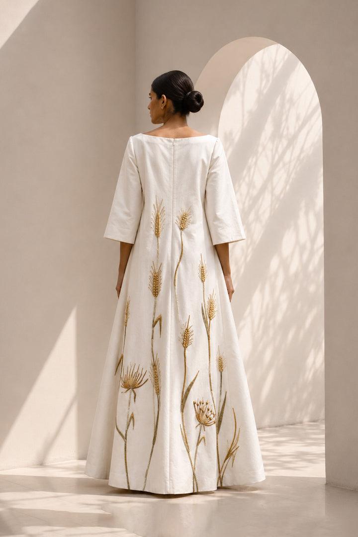 Ivory column gown adorned with delicate botanical embroidery. Featuring elegant boat-neckline, relaxed three-quarter sleeves &amp; flowing back panel.