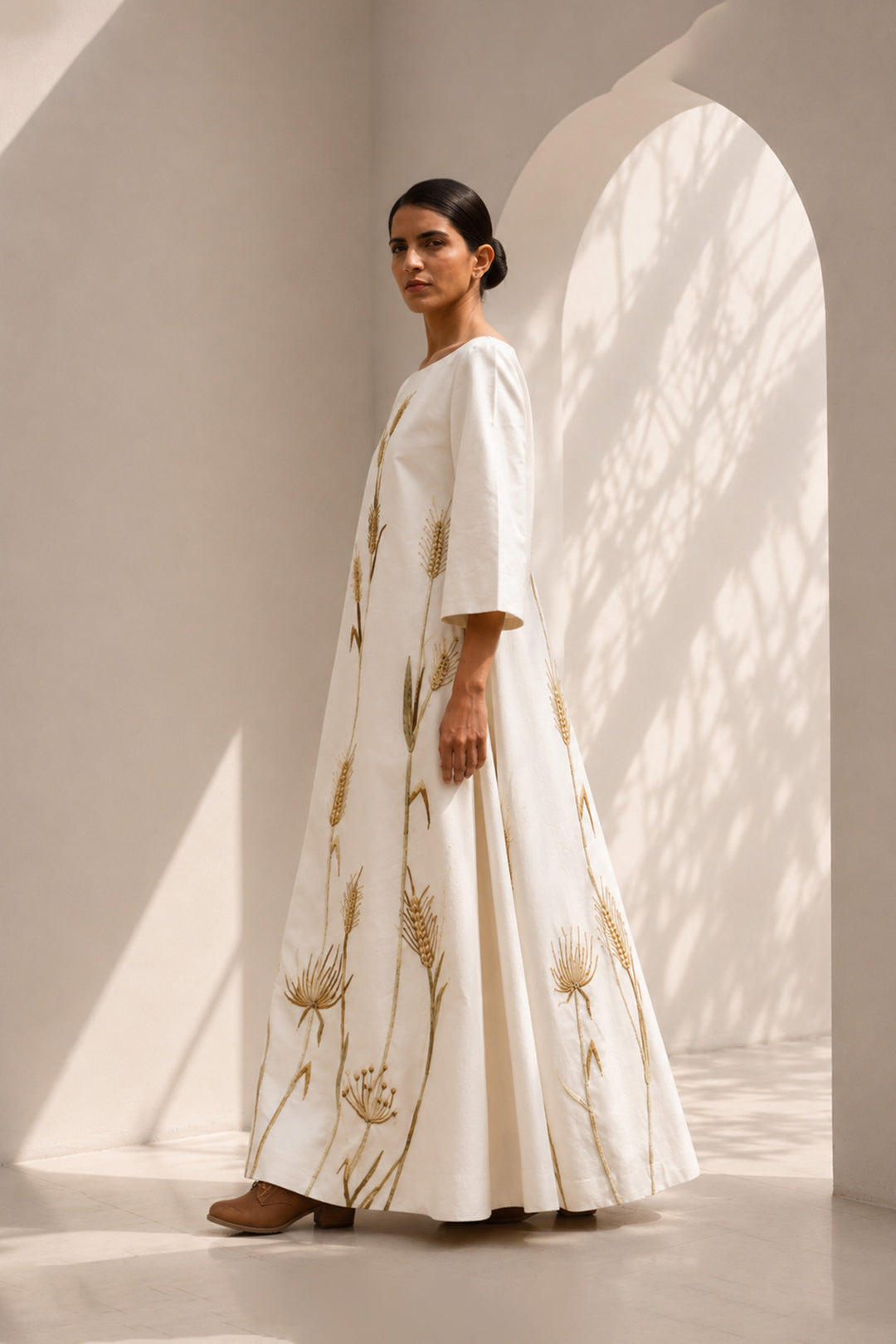 Ivory column gown adorned with delicate botanical embroidery. Featuring elegant boat-neckline, relaxed three-quarter sleeves &amp; flowing back panel.