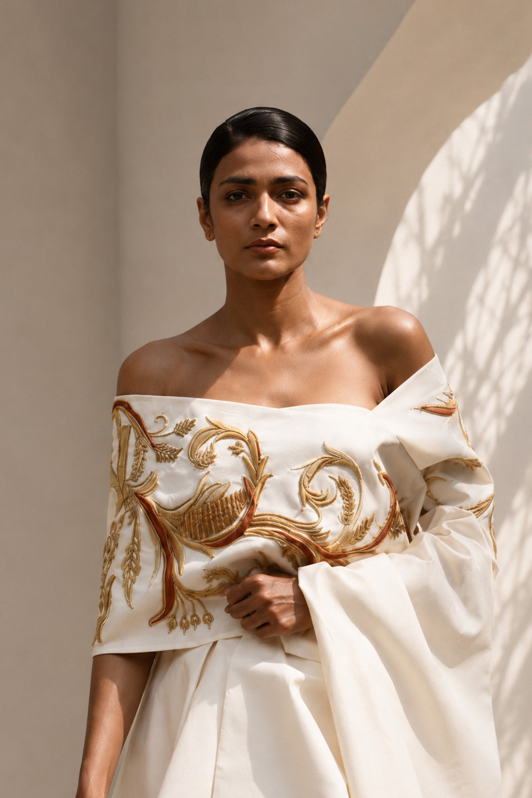 Ivory draped ensemble featuring off-shoulder embroidered stole, sculptural layering.