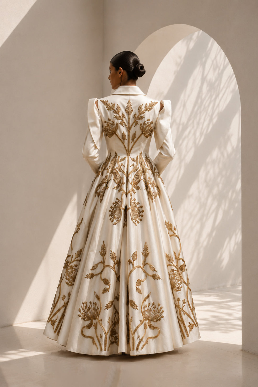 Ivory embroidered gown featuring a tailored blazer-inspired bodice with sculptural cut-out sleeves and voluminous flare.