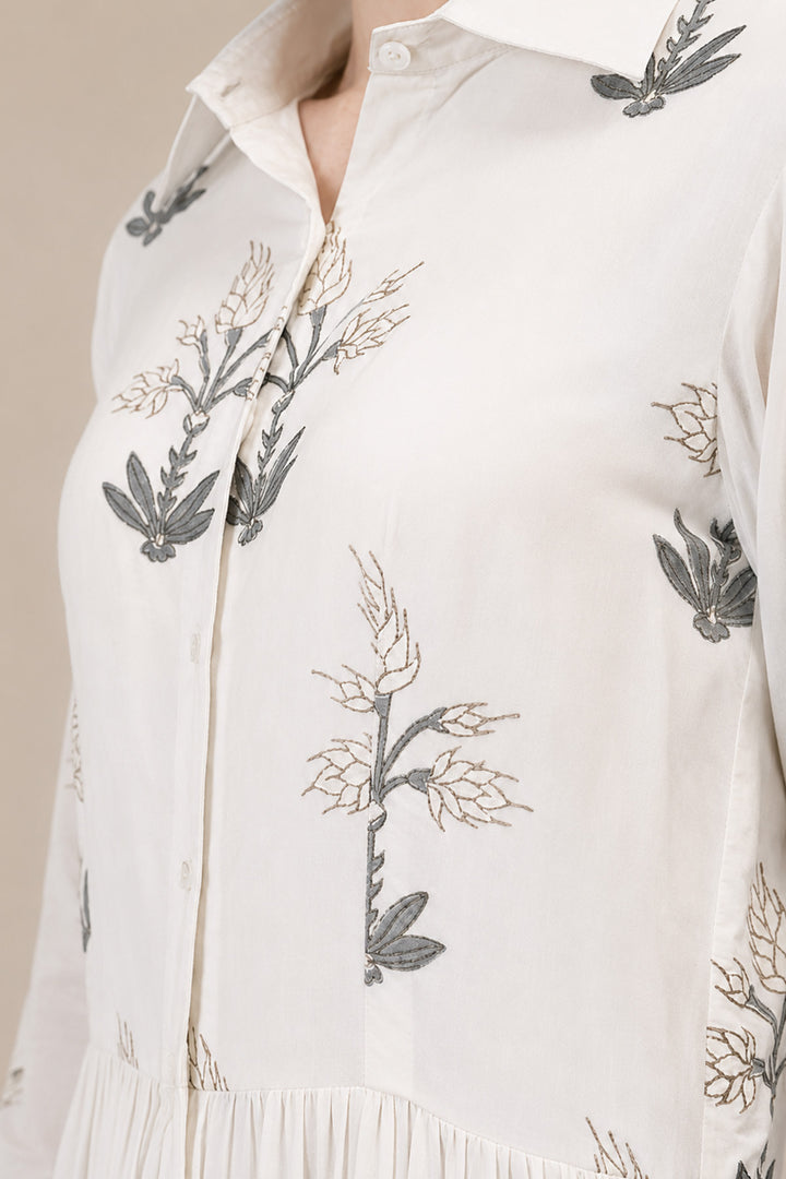 Ivory shirt dress adorned with delicate botanical prints, featuring a structured collar and cascading tiered silhouette.