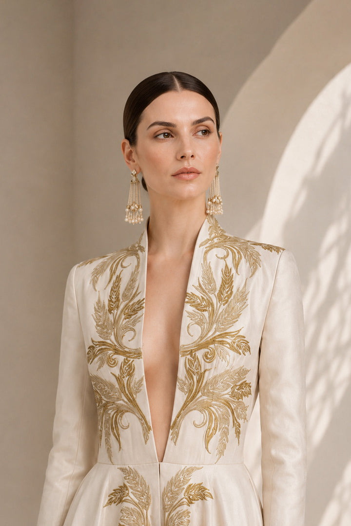 Ivory embroidered gown featuring an architectural plunging neckline, full-sleeved, structured bodice, voluminous flared hem.