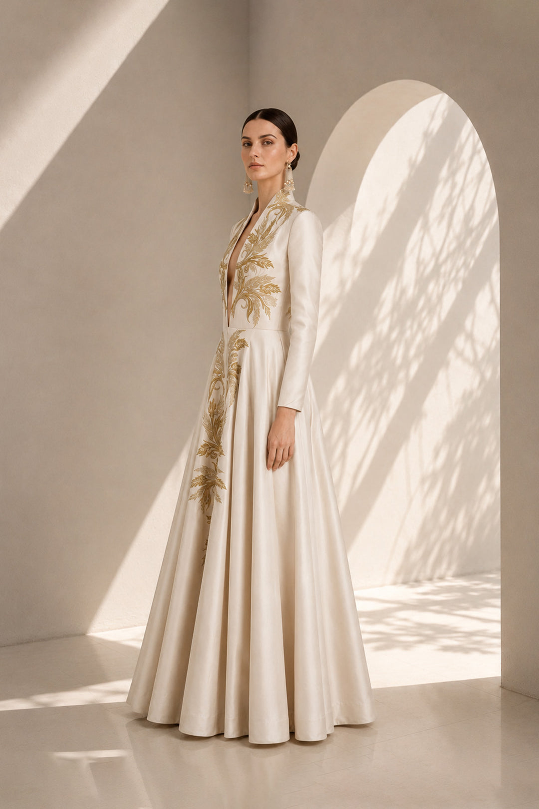 Ivory embroidered gown featuring an architectural plunging neckline, full-sleeved, structured bodice, voluminous flared hem.
