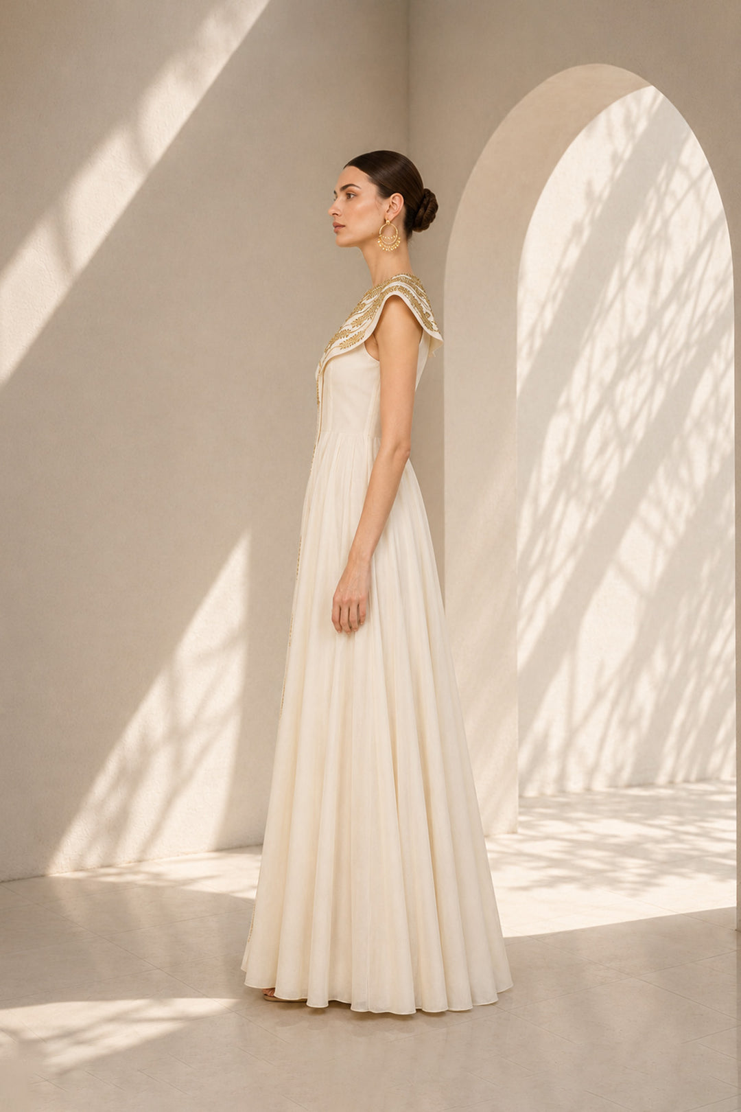Ivory floor-length gown adorned with intricate embroidery, sculptural cape collar,vertical embroidered front panel for an elongated look.