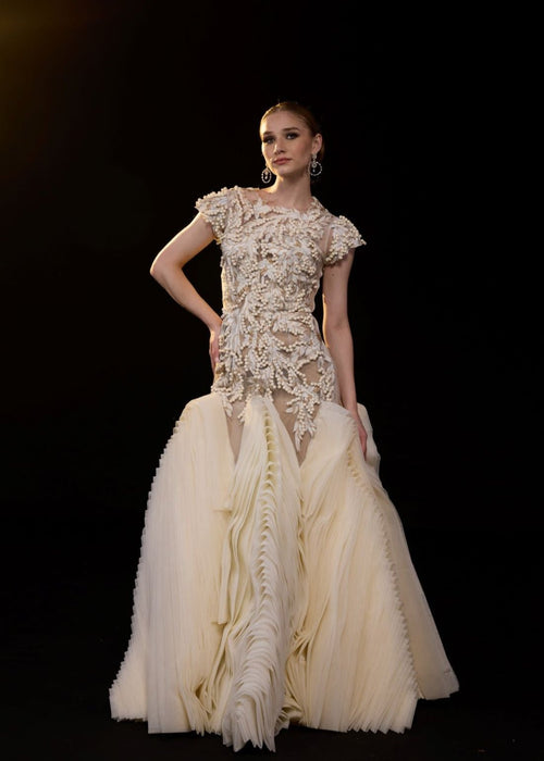 A elegant gown features a sheer, cap-sleeve bodice adorned with intricate 3D floral embellishment.