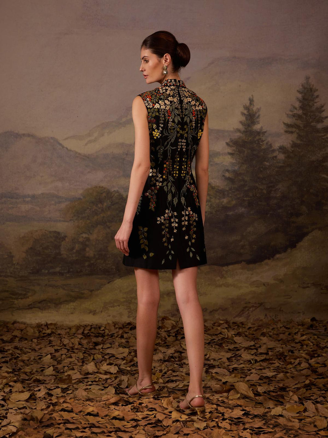 A sleeveless black mini dress features a high neckline and vibrant floral embroidery.