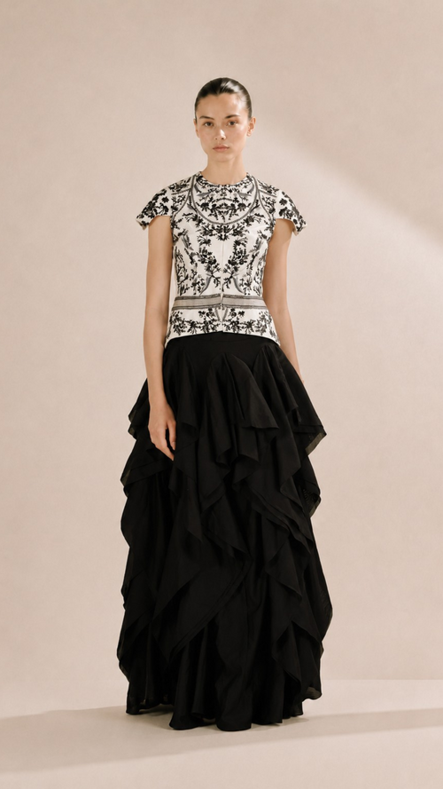 Woman wearing a black and white patterned top with a black ruffled skirt on a beige background