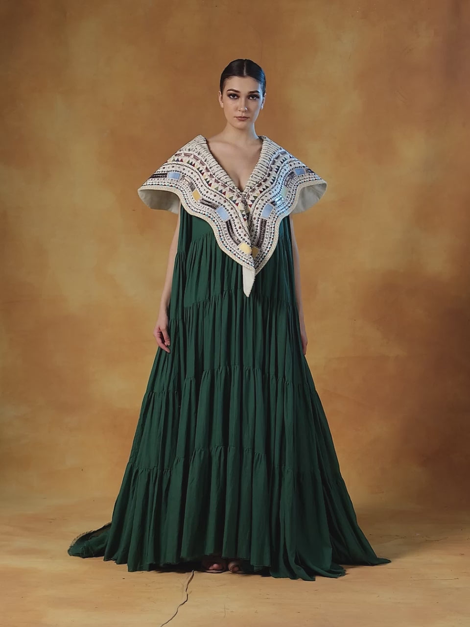 Floor length cotton tier dress in olive green. It is topped with a heavy embroidered cape around the neckline and shoulders.