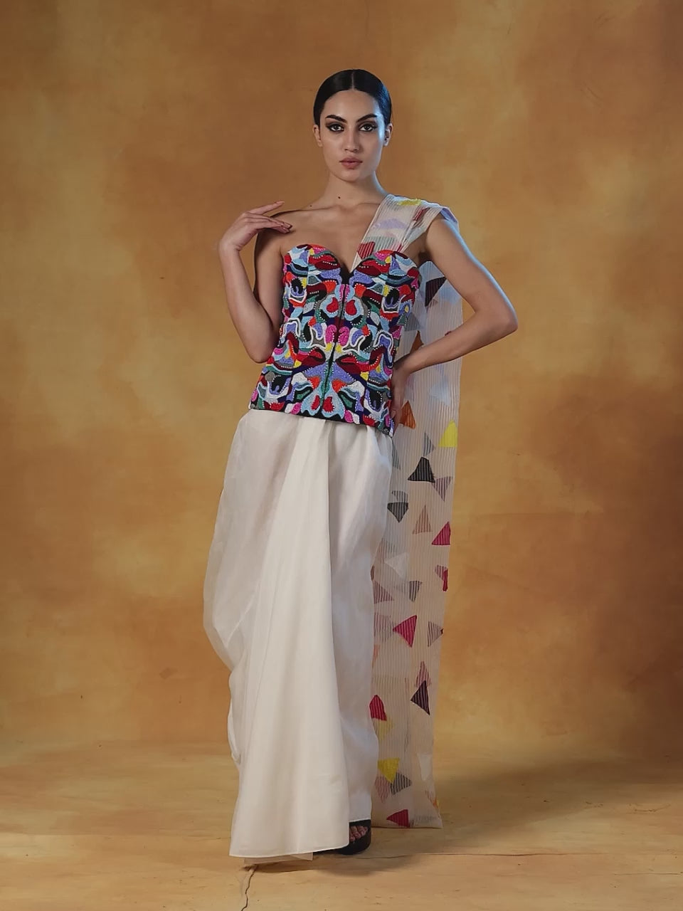 Corset that is intricately embroidered in colorful beads, decorated with a printed pallu and is paired with a plain white cotton silk drape skirt.